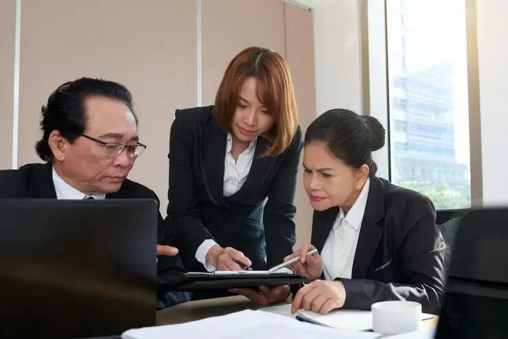 Three businesspeople review documents, conducting AML/CTF ongoing customer due diligence (OCDD).