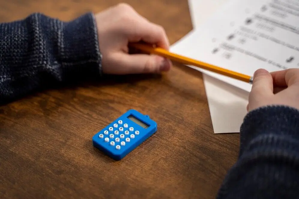 Close-up of a child's hands using a calculator and pencil on a test, demonstrating the importance of financial literacy and AML compliance.