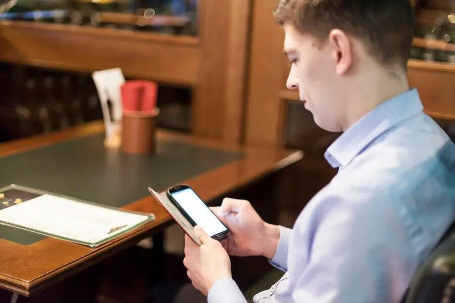 Man reviewing a document on his phone at a restaurant table.