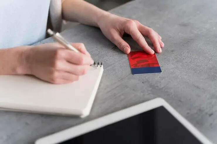 Person writing notes and reviewing a red and blue card, possibly for AML/CTF ongoing customer due diligence (OCDD).