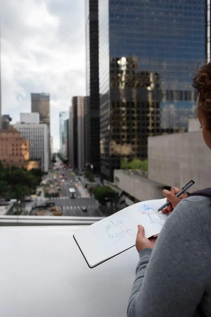 Person sketching city skyline while working on a notepad.