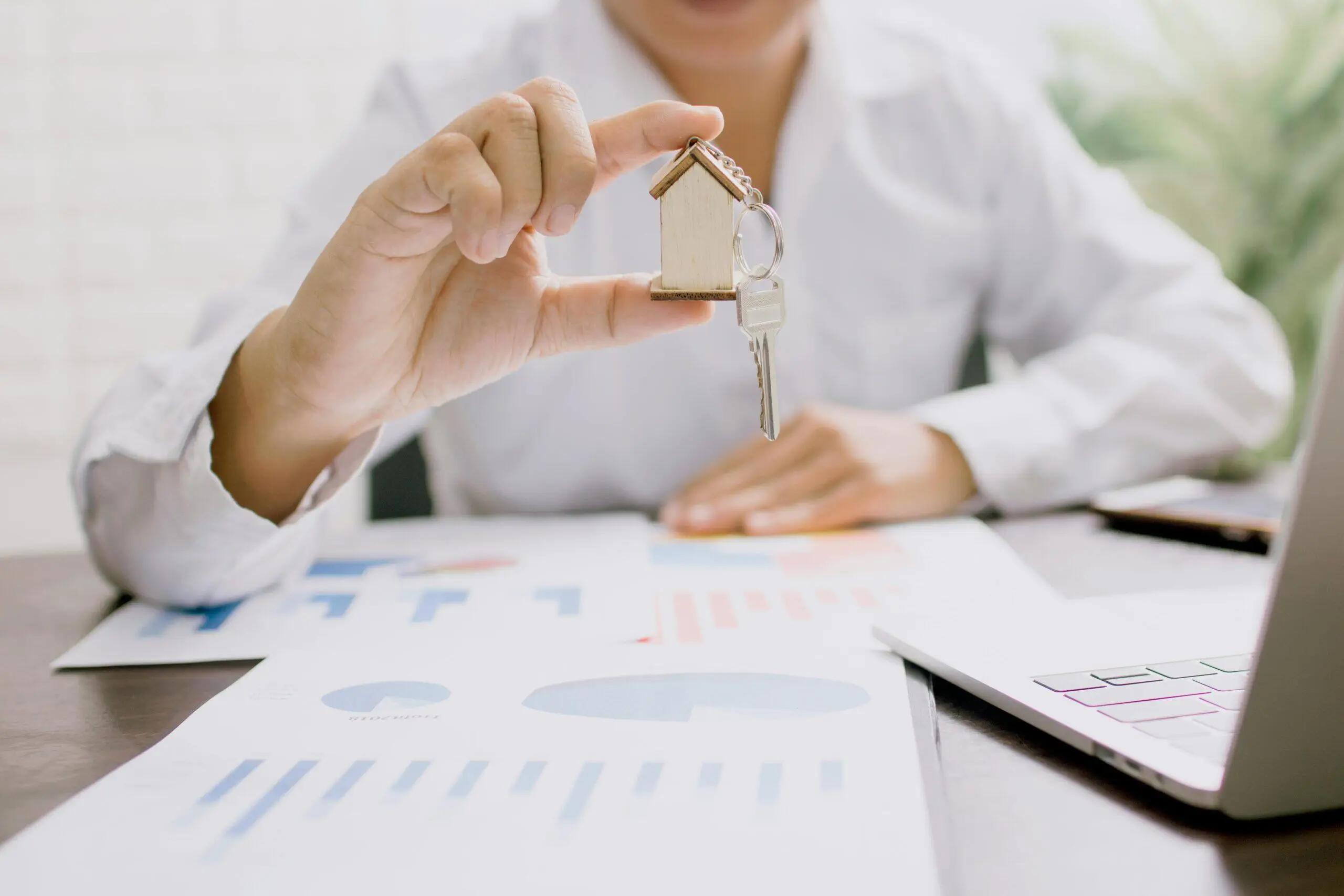 Person holding house key and miniature house model.
