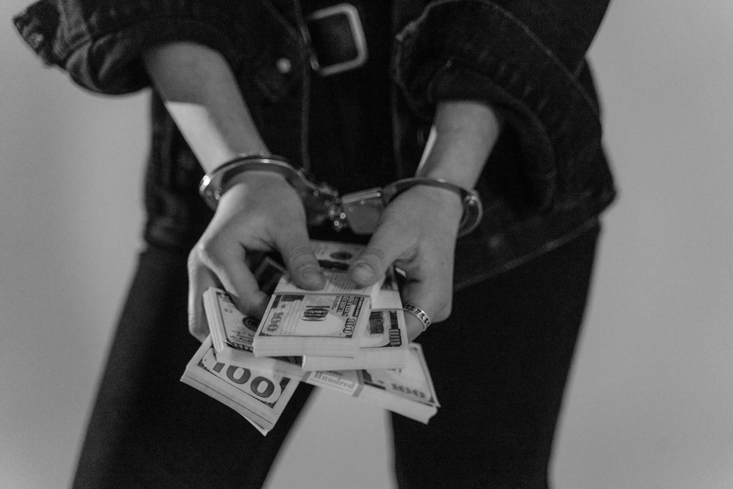 Person in handcuffs holding a stack of US $100 bills. Money laundering prevention.